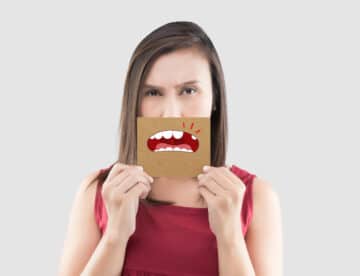 Asian woman in the red shirt holding a brown paper with the broken tooth cartoon picture of his mouth against the gray background, Decayed tooth, The concept with healthcare gums and teeth
