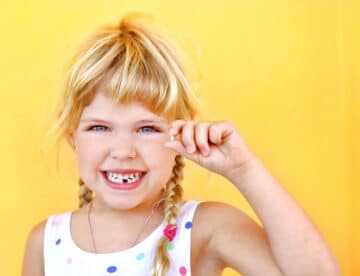 Smiling girl holding missing tooth