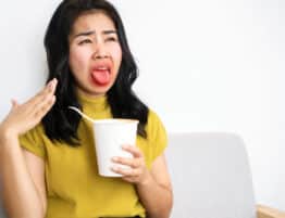 Asian woman eating very hot and spicy noodle from a cup her mouth and tongue burning and red