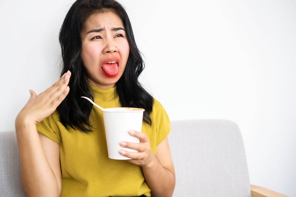 Asian woman eating very hot and spicy noodle from a cup her mouth and tongue burning and red