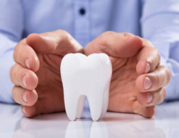 Man's Hand Protecting Healthy Hygienic White Tooth On Reflective Table