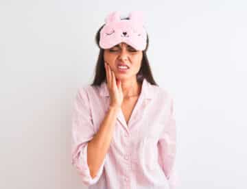 Young beautiful woman wearing sleep mask and pajama over isolated white background touching mouth with hand with painful expression because of toothache